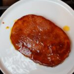 Fully cooked brown sugar dijon glazed ham steak on a white plate.