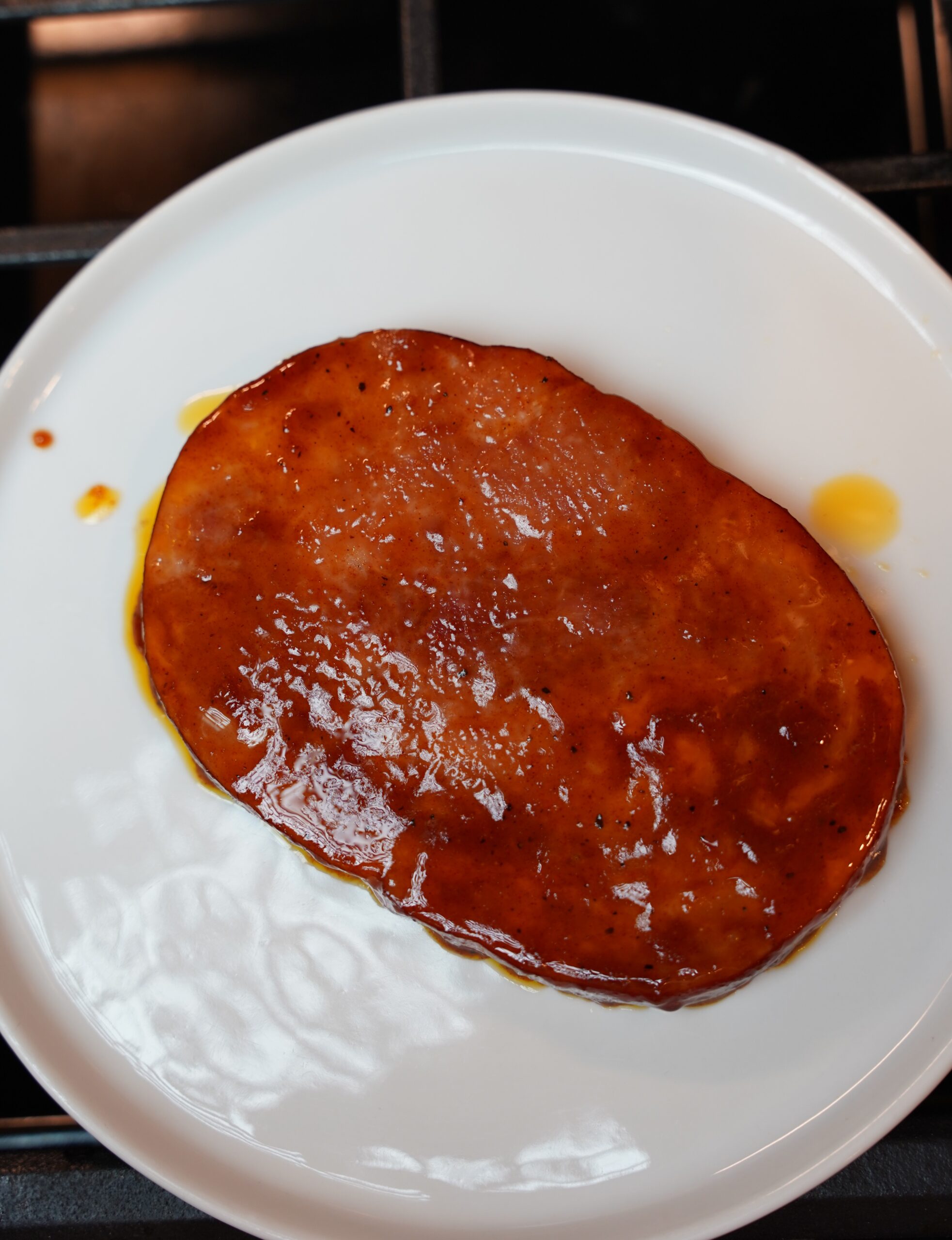 Fully cooked brown sugar dijon glazed ham steak on a white plate.