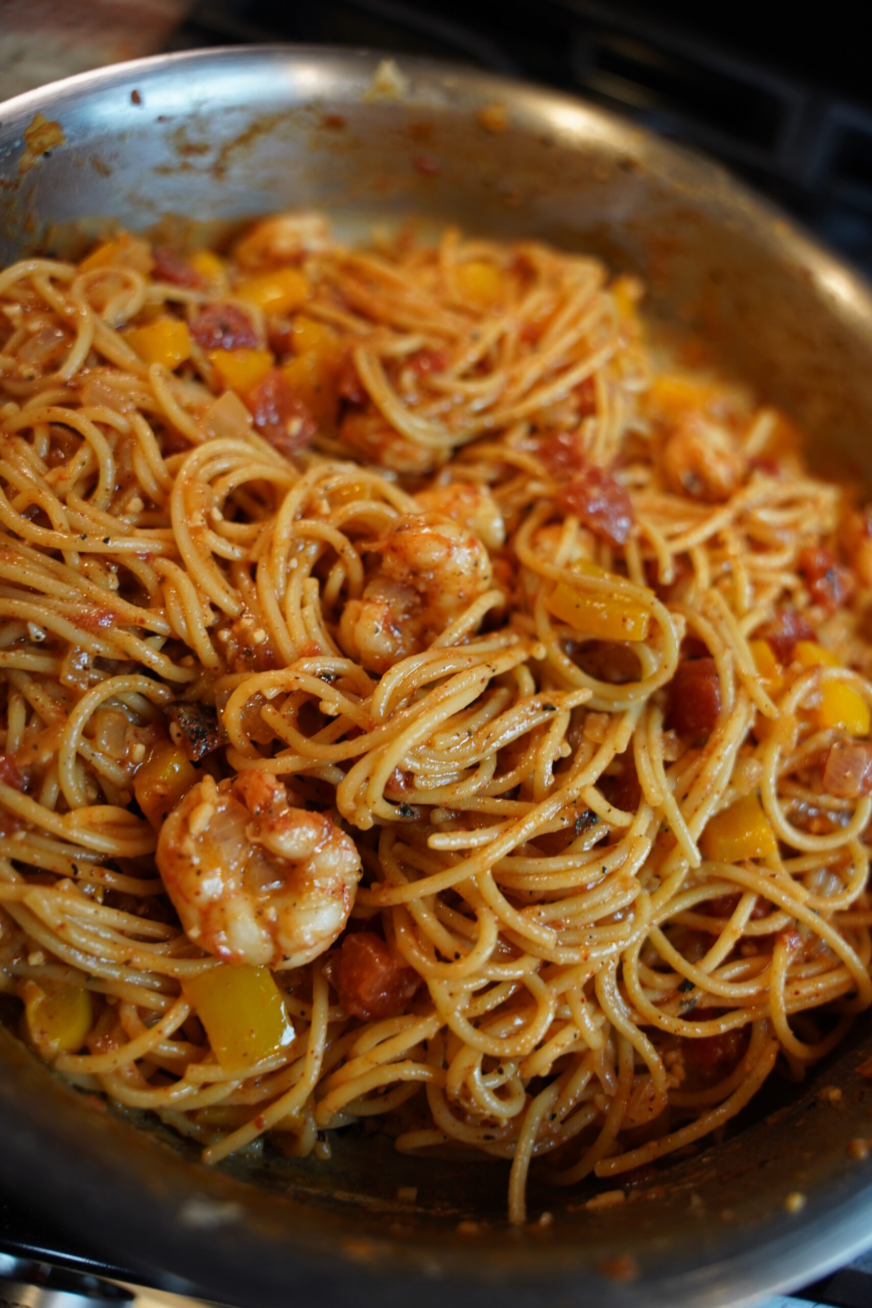 Cajun shrimp pasta in a pan. deep red sauced noodles with boiled shrimp, onion, bell pepper, garlic and seasonings.