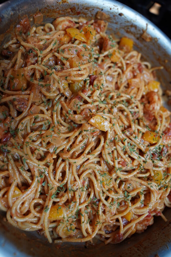 Cajun shrimp pasta in a large pan topped with finely minced parsley. deep red sauced noodles with boiled shrimp, onion, bell pepper, garlic and seasonings.