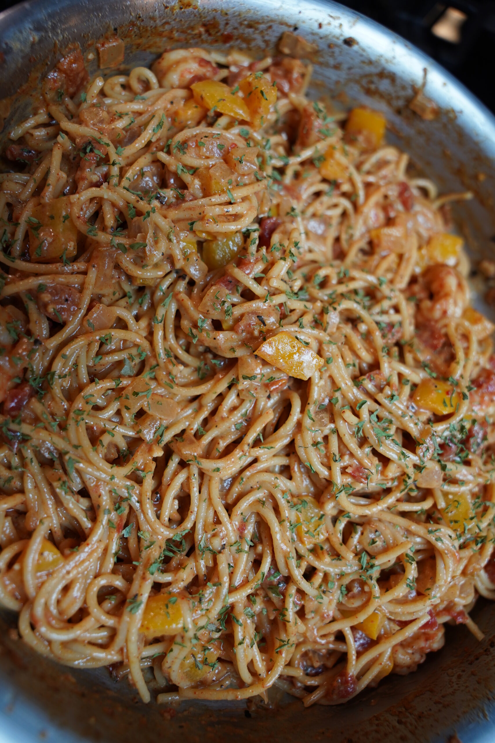 Cajun shrimp pasta in a large pan topped with finely minced parsley. deep red sauced noodles with boiled shrimp, onion, bell pepper, garlic and seasonings.