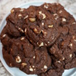 Double Chocolate Macadamia Nut Cookies baked and sitting on a white plate on a granite countertop.