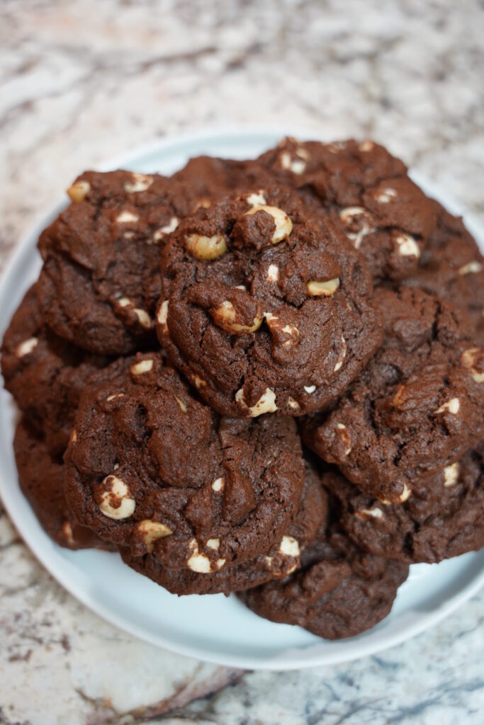 Double Chocolate Macadamia Nut Cookies baked and sitting on a white plate on a granite countertop.