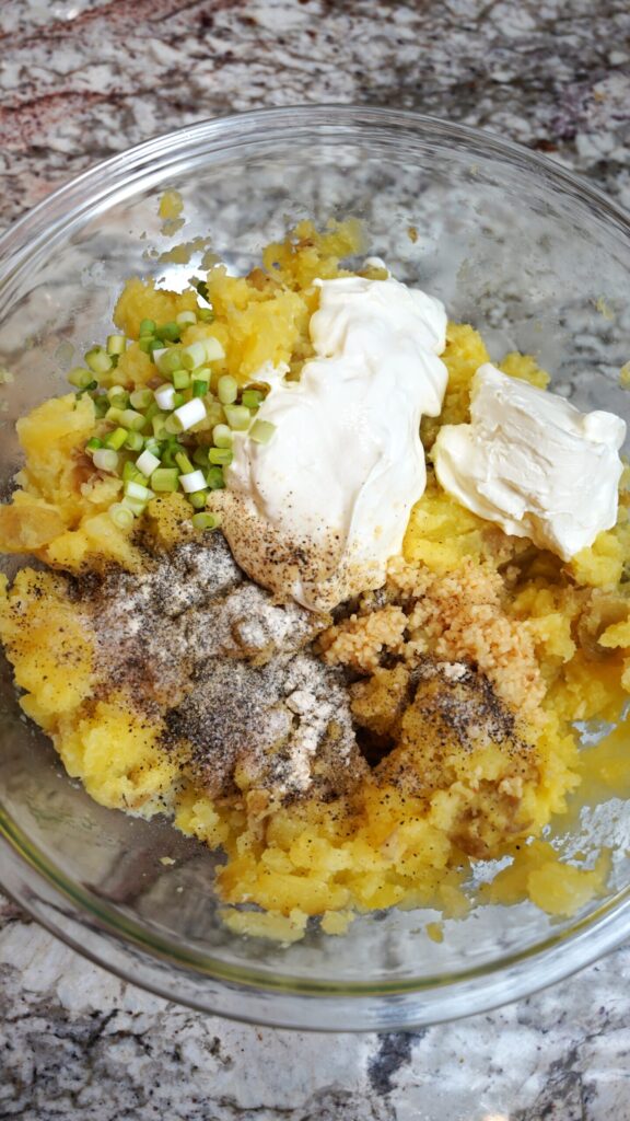 Mashed yukon gold potatoes with seasonings (salt, pepper, onion powder), green onion, butter, garlic, milk, sour cream, and cream cheese - all ready for mixing. Chef level mashed potatoes ingredients.