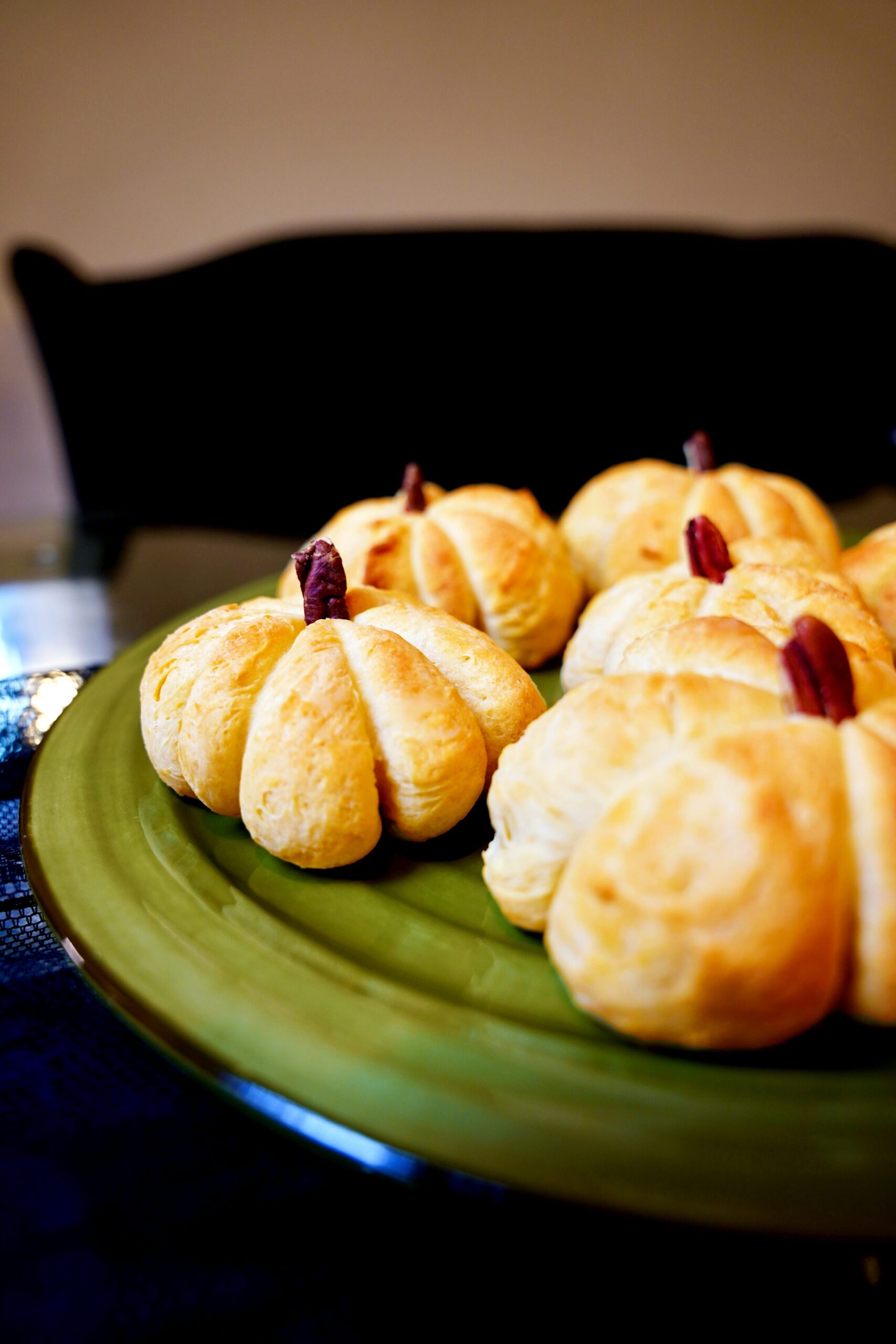 Cute and festive pumpkin shaped dinner rolls on a large green plate, holiday side.