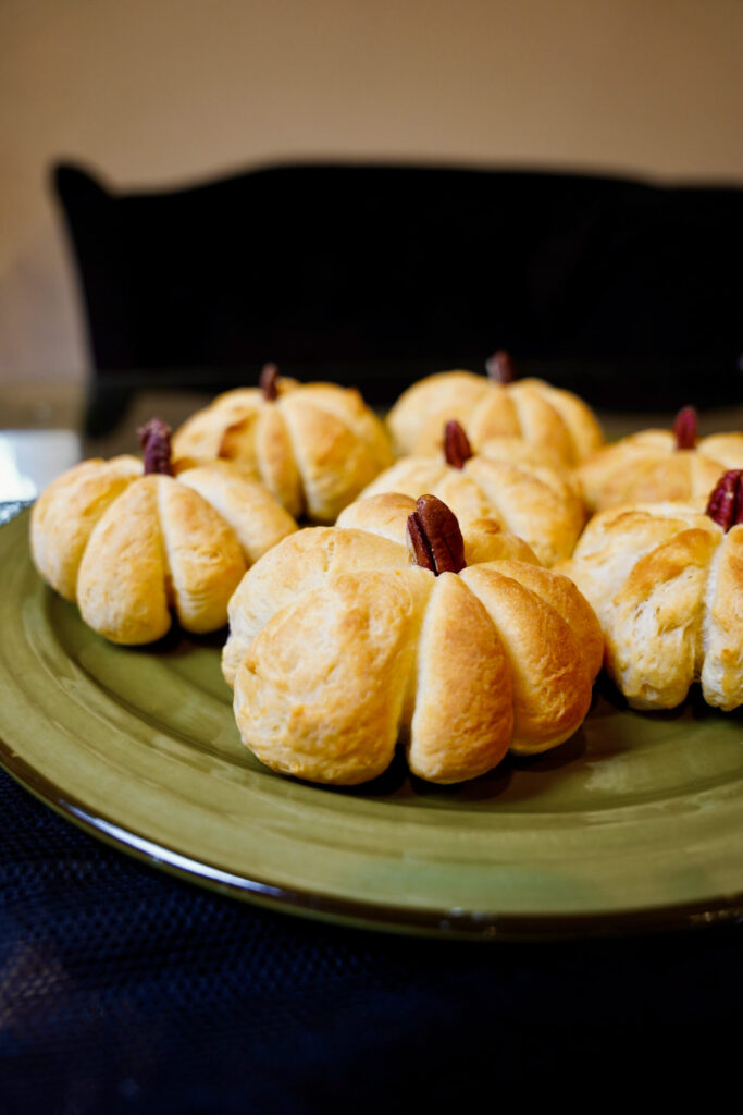 Delicious pumpkin shaped dinner rolls on a green plate. Warm, golden bread recipe.