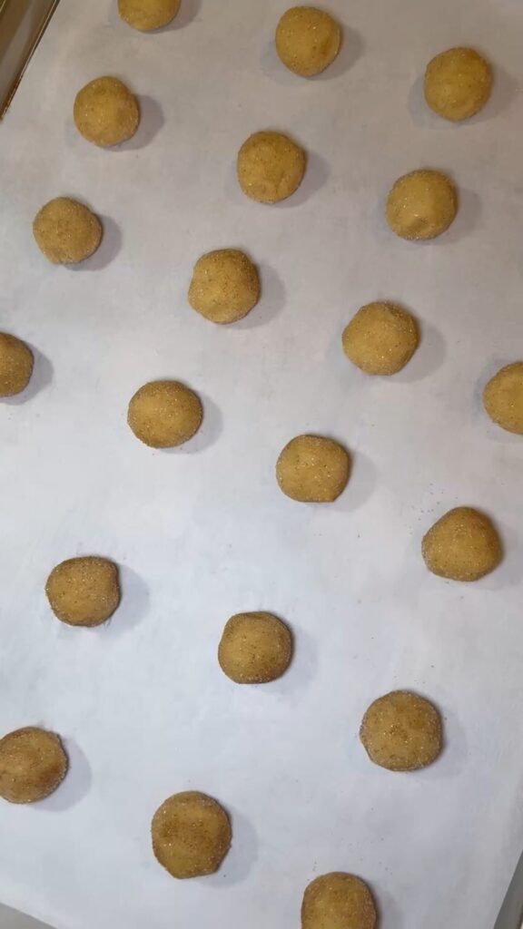 Snickerdoodle cookie dough balls on a sheet pan, rolled in cinnamon sugar and ready for baking