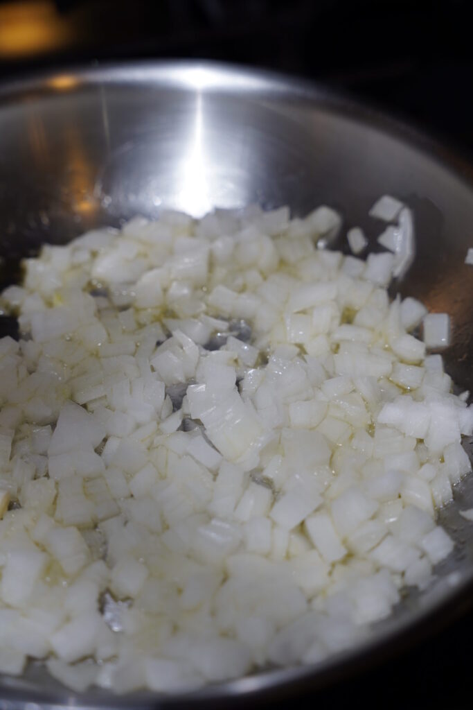 Onions cooking in a stainless steel pan with olive oil.