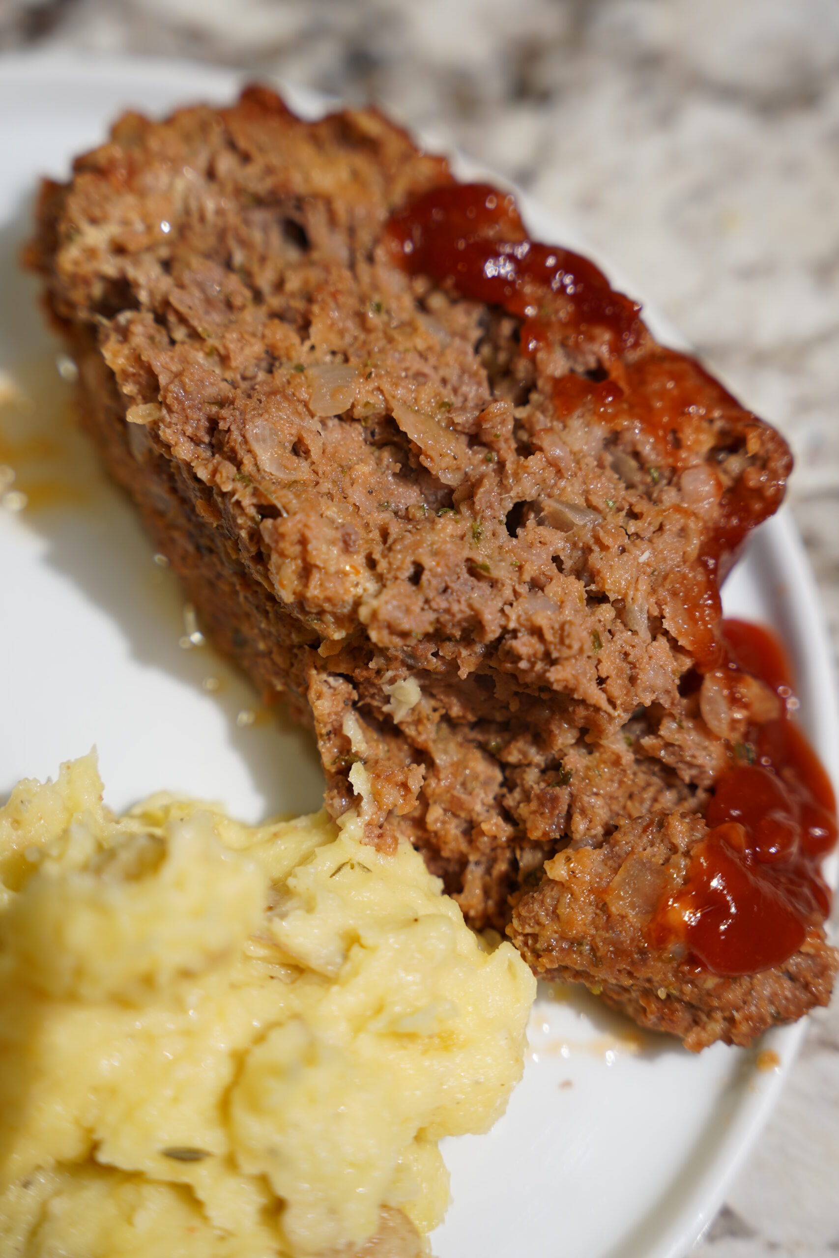 Meatloaf and Brown Butter Mashed Potatoes on a white plate sitting on a granite countertop