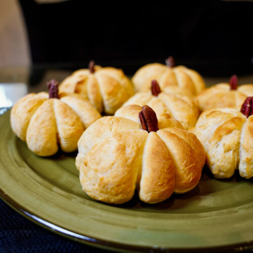 Delicious pumpkin shaped dinner rolls on a green plate. Warm, golden bread recipe.